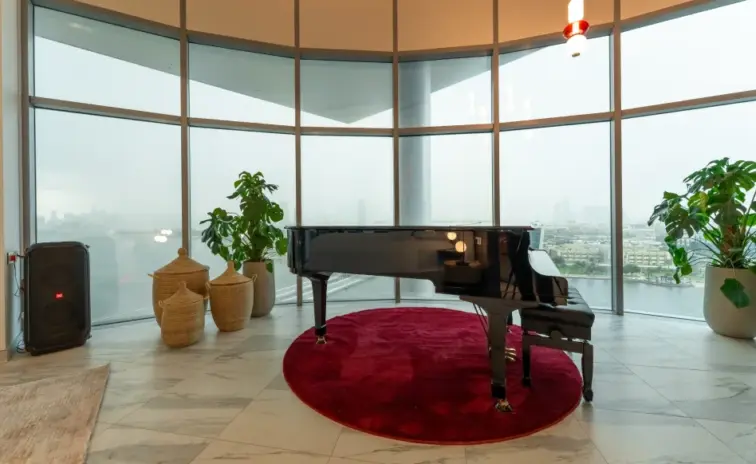 grand piano on a red rug beside curved floor to ceiling windows